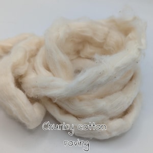 Könnte beinhalten: Nahaufnahme eines Haufens cremefarbener, grober Baumwollroving. Die weichen, strukturierten Fasern sind locker angeordnet und erzeugen ein flauschiges Aussehen. Der Text "Chunky cotton roving" ist in schwarzer, handschriftlicher Schrift am unteren Bildrand geschrieben.