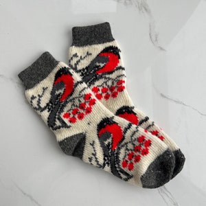 Puede incluir: Un par de calcetines de punto blanco con un puño gris. Los calcetines presentan un patrón de petirrojos rojos y bayas rojas sobre un fondo blanco.