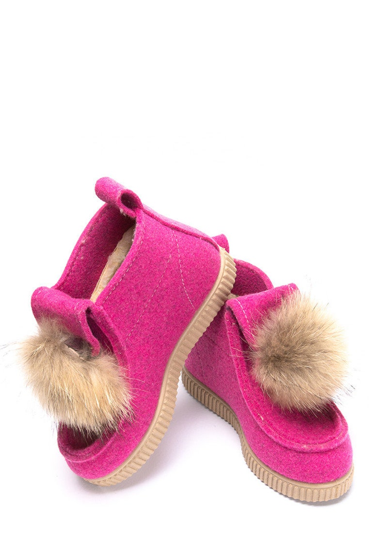 May include: A pair of pink felt boots with brown fur pom-poms. The boots have a rubber sole.
