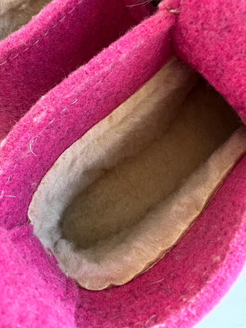 May include: Close-up of the inside of a pink felt slipper with a beige fleece lining.
