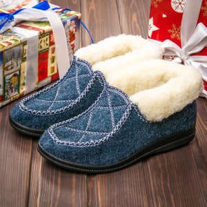 Puede incluir: Un par de zapatillas de estar por casa acolchadas de color azul con forro de borreguito blanco. Las zapatillas tienen una suela de goma negra.