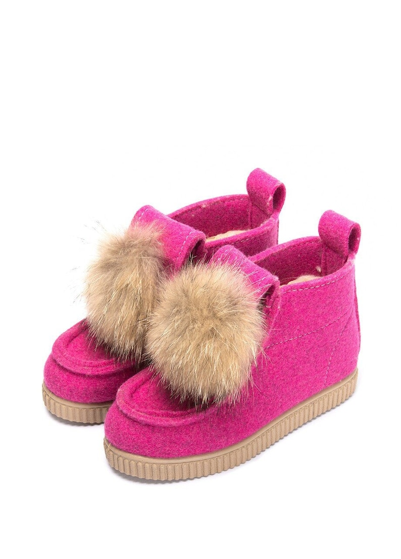 May include: Pink felt boots with brown fur pom-poms. The boots have a rubber sole and a pull-on style.