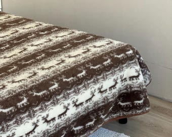 Peut inclure: Une couverture marron et blanche à motifs de rennes répétés. La couverture est drapée sur un lit, mettant en valeur sa texture et sa palette de couleurs. Le motif est un motif répété de silhouettes de rennes.