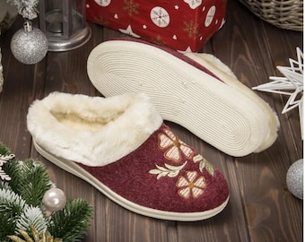 Pode incluir: Um par de pantufas bordô com forro de pele sintética branca e desenhos florais bordados. As pantufas têm uma sola de borracha branca.