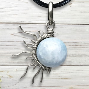 May include: A silver pendant necklace with a light blue gemstone in the center, surrounded by a silver sunburst design.