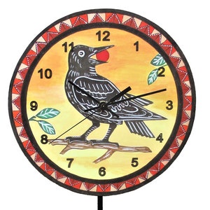 May include: A round wall clock with a yellow background featuring a black bird perched on a branch holding a red berry. The clock face has black numbers and hands, surrounded by a red and white triangular border. A flower-shaped pendulum hangs below.