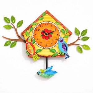 May include: A whimsical, hand-painted cuckoo clock featuring a yellow house with a clock face and two colorful birds perched on branches with green leaves. A small bird hangs below. The clock is a decorative wall hanging.