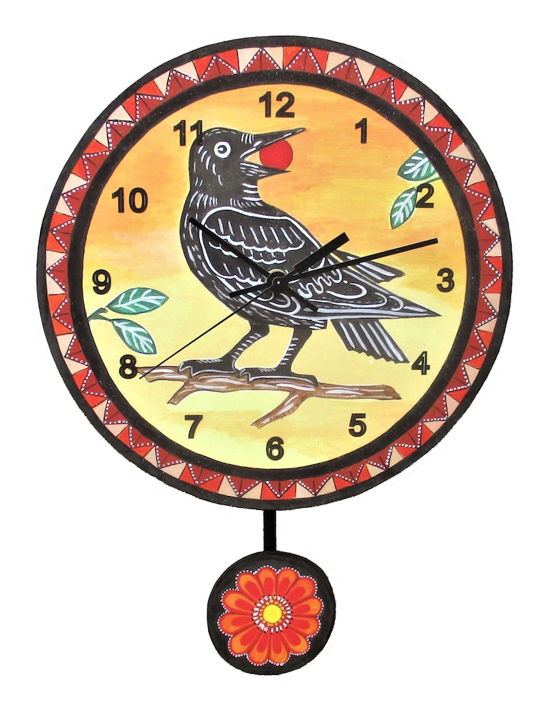 May include: A round wall clock with a yellow background featuring a black bird perched on a branch holding a red berry. The clock face has black numbers and hands, surrounded by a red and white triangular border. A flower-shaped pendulum hangs below.
