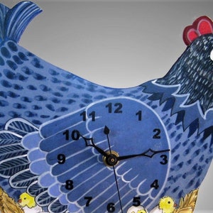 May include: A whimsical blue hen-shaped wall clock. The clock face is integrated into the hen's body, with black hands indicating the time. The hen has a red comb, white face, and yellow chicks at the bottom. The clock is painted with a folk art style.