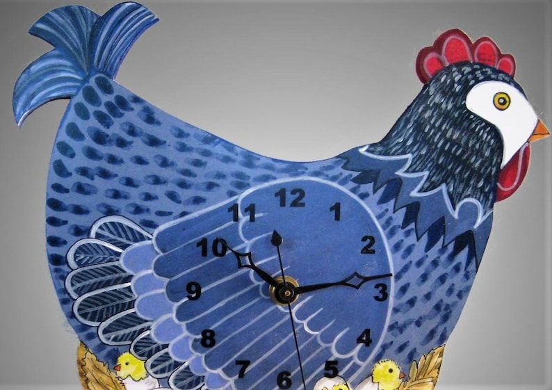 May include: A whimsical blue hen-shaped wall clock. The clock face is integrated into the hen's body, with black hands indicating the time. The hen has a red comb, white face, and yellow chicks at the bottom. The clock is painted with a folk art style.