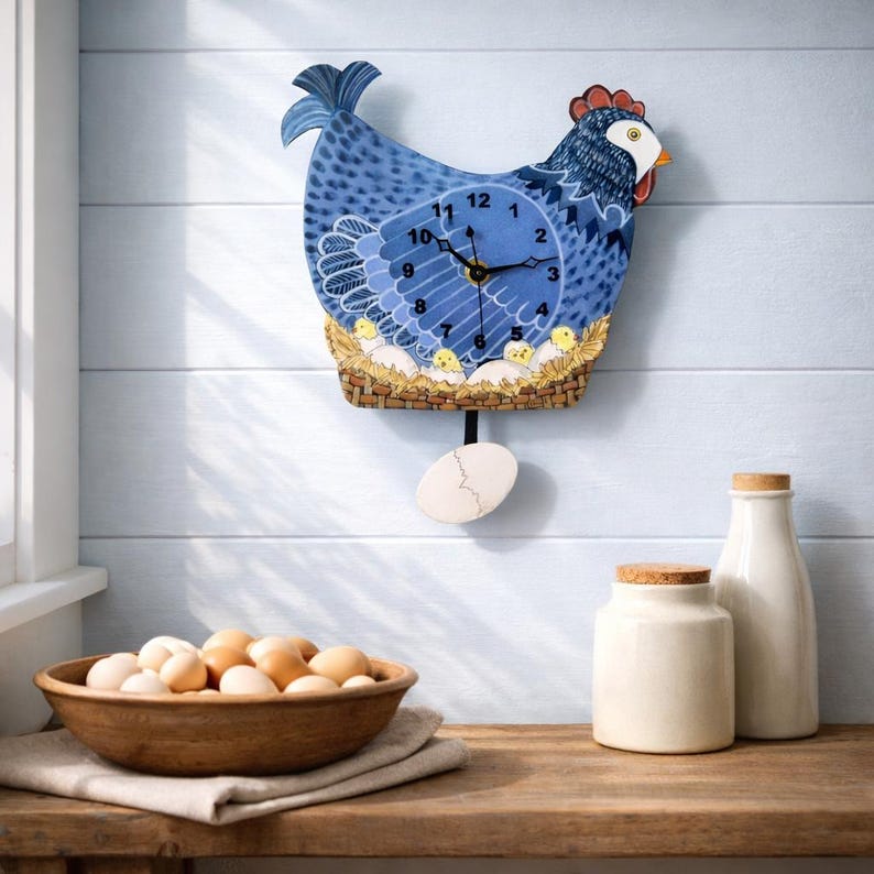 May include: A blue chicken-shaped wall clock with a pendulum egg. The clock face is blue with black hands and white numbers. A wooden bowl of eggs and two white ceramic containers sit on a wooden surface.