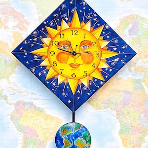 May include: A whimsical wall clock featuring a smiling sun face with a yellow and orange design, set against a blue starry background. The clock has black hands and a pendulum with a globe design. The clock is approximately 12 inches in height.