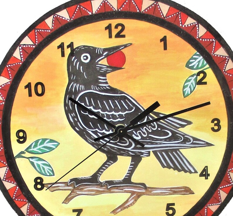 May include: A round wall clock with a yellow and orange gradient background featuring a black bird perched on a branch holding a red berry in its beak. The clock face has black numbers from 1 to 12 and a decorative red and white triangular border.