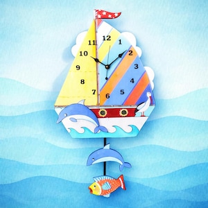 May include: A nautical-themed wall clock shaped like a sailboat. The clock features a yellow, blue, and orange striped sail, a red flag, and a white hull with a dolphin and seagull. Additional hanging dolphins and a fish complete the design.