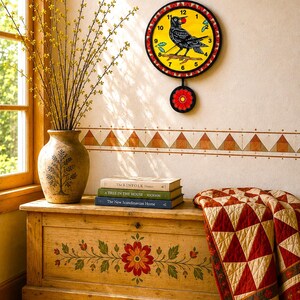 May include: A round wall clock with a yellow face featuring a black bird holding a red berry, surrounded by a red and white patterned border. Below the clock hangs a circular pendulum with a red flower design on a black background.