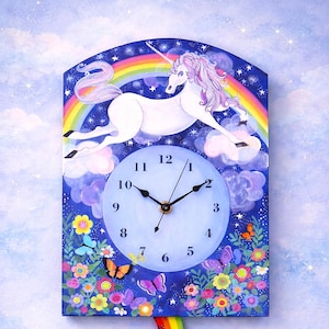 May include: A whimsical wall clock featuring a white unicorn with a pink mane and a rainbow. The clock face is light blue with black hands. Colorful flowers and butterflies decorate the bottom. The clock is approximately 12 inches tall.