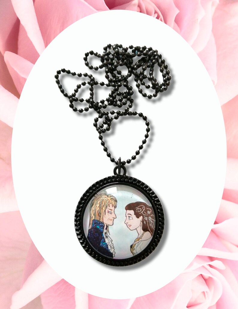 May include: A black chain necklace with a round glass pendant featuring a black and white illustration of a man and woman looking at each other.
