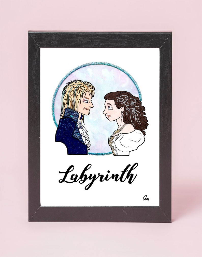 May include: A framed illustration of two characters from the movie Labyrinth. The characters are a man with long blonde hair and a woman with long brown hair. They are standing in front of a blue and purple circle with a sparkly border. The text "Labyrinth" is written in black cursive below the characters.