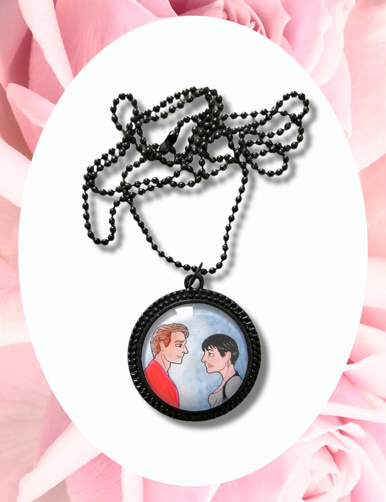 May include: A black chain necklace with a round glass pendant featuring a hand-painted illustration of two people looking at each other. The pendant has a black metal frame.