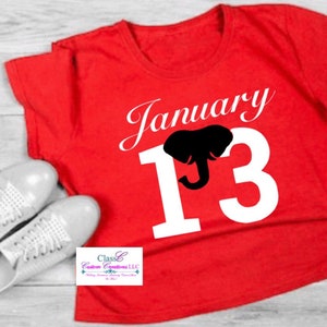 May include: Red t-shirt with white text that says "January 13" with a black elephant silhouette in the middle of the number 13.
