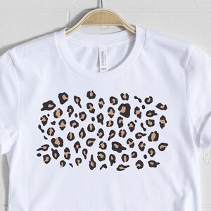 May include: White t-shirt with a brown and black leopard print design.