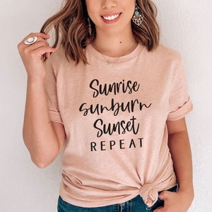 May include: A light pink t-shirt with the text "Sunrise Sunburn Sunset Repeat" in black lettering.