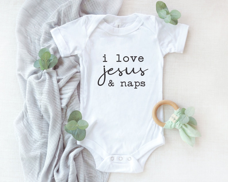 May include: White baby onesie with black text that reads "i love jesus & naps".