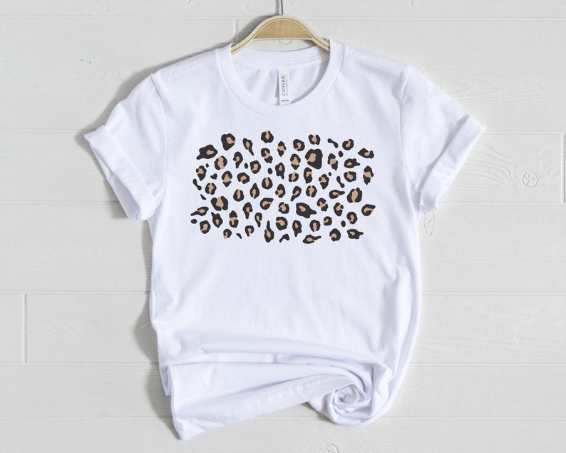 May include: White t-shirt with a brown and black leopard print design.