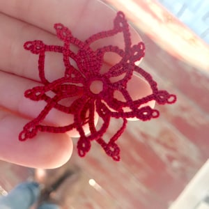 Puede incluir: Un copo de nieve de ganchillo rojo con un diseño delicado e intrincado.