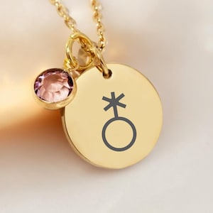 May include: Gold necklace with a round pendant featuring a gender-neutral symbol and a small pink crystal charm.