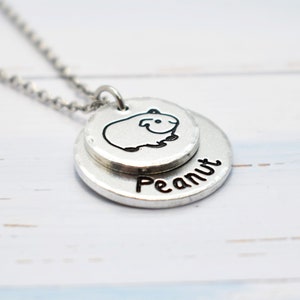 May include: A silver necklace with a charm featuring a small guinea pig and the name "Peanut" engraved on the bottom.