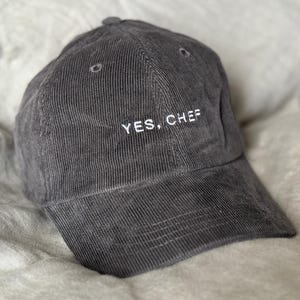 May include: A gray corduroy baseball cap with the embroidered text "YES, CHEF" in white. The hat has a curved brim and a structured crown. The hat is a casual accessory.