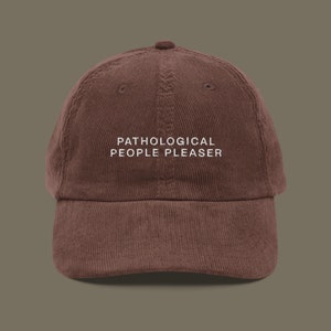 Puede incluir: Una gorra de béisbol de pana marrón con texto bordado en blanco que dice "Pathological People Pleaser".