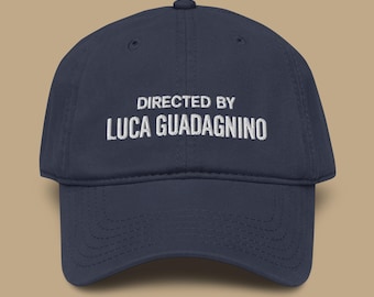 Op de afbeelding: Marineblauwe baseballcap met de witte, geborduurde tekst "DIRECTED BY LUCA GUADAGNINO". De cap heeft een gebogen klep en een verstelbare band. Een modieus accessoire voor filmliefhebbers.