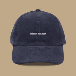 May include: A navy blue corduroy baseball cap with white embroidery that reads "BIRD NERD".