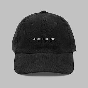 May include: Black corduroy baseball cap with the text "ABOLISH ICE" embroidered in white across the front. The cap has a curved brim and a rounded crown. The hat is a classic six-panel design.