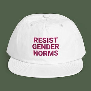 Könnte beinhalten: Eine weiße Baseballkappe mit strukturierter Krone und flachem Schirm. Auf der Vorderseite der Kappe befindet sich der Text RESIST GENDER NORMS, der in einer fetten, dunkelmagentafarbenen serifenlosen Schrift gedruckt ist. Die Kappe hat Belüftungsösen.