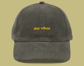 May include: A dark green corduroy baseball cap with the text "gay vibes" embroidered in yellow.