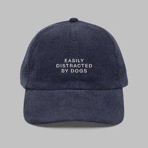 May include: A navy blue corduroy baseball cap with white embroidery that reads "EASILY DISTRACTED BY DOGS".