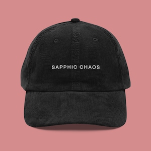 Könnte beinhalten: Eine schwarze Baseballkappe aus Cord mit weiß gesticktem Text, der "SAPPHIC CHAOS" lautet.