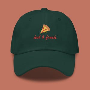 May include: A dark green baseball cap with an embroidered image of a pizza slice and the text "hot & fresh" in red.