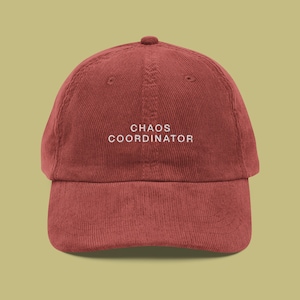 May include: A burgundy corduroy baseball cap with white embroidered text that reads "CHAOS COORDINATOR".