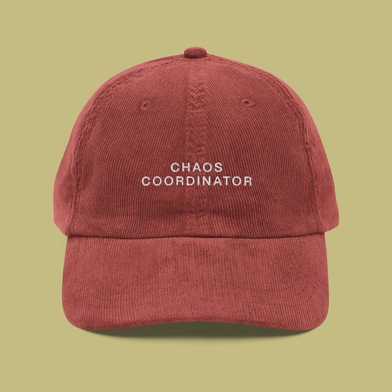 May include: A burgundy corduroy baseball cap with white embroidered text that reads "CHAOS COORDINATOR".