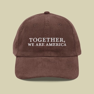 Könnte beinhalten: Braune Cord-Baseballkappe mit dem gestickten Text "TOGETHER, WE ARE AMERICA" in Weiß. Die Kappe hat einen gebogenen Schirm und eine abgerundete Oberseite.