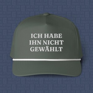 May include: A dark olive green baseball cap featuring a white cord trim across the base of the crown. The front of the cap displays the embroidered white text "ICH HABE IHN NICHT GEWÄHLT" in a clean, sans-serif font centred on the front panel.