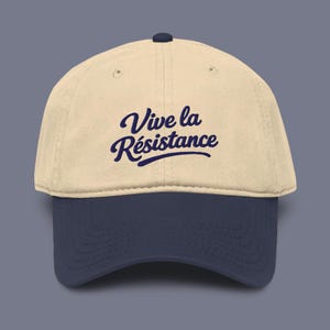 Puede incluir: Gorra de béisbol beige con visera azul marino. La gorra presenta el texto "Vive la Résistance" en escritura azul marino. La gorra tiene una visera curva y un botón en la parte superior.