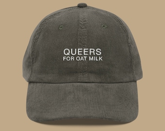 May include: An olive green corduroy baseball cap with the embroidered text "QUEERS FOR OAT MILK" in white. The cap has a curved peak and an adjustable strap at the back. The hat is a casual accessory.