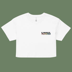 Puede incluir: Camiseta blanca recortada con un logotipo negro de U-Haul y el texto "A Proud Team Member" con una franja arcoíris debajo.