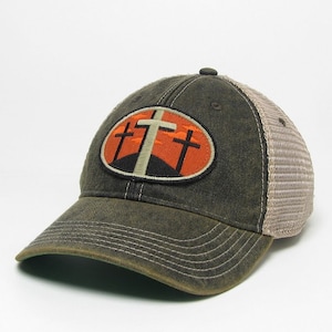 May include: A black and brown baseball cap with a mesh back. The front of the cap features an embroidered patch with three white crosses on an orange background.