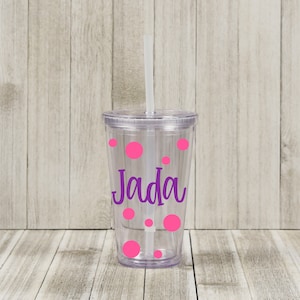 May include: A clear plastic tumbler with a pink polka dot design and the name "Jada" in purple lettering. The tumbler has a straw.